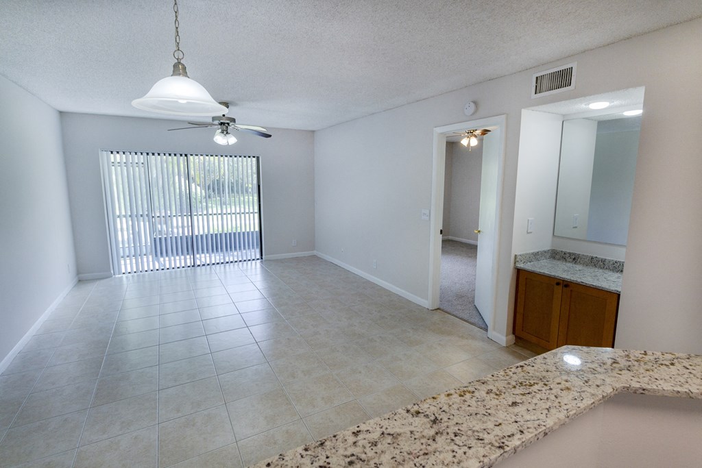 A room with a fan, a window with blinds, a mirror, and a counter.